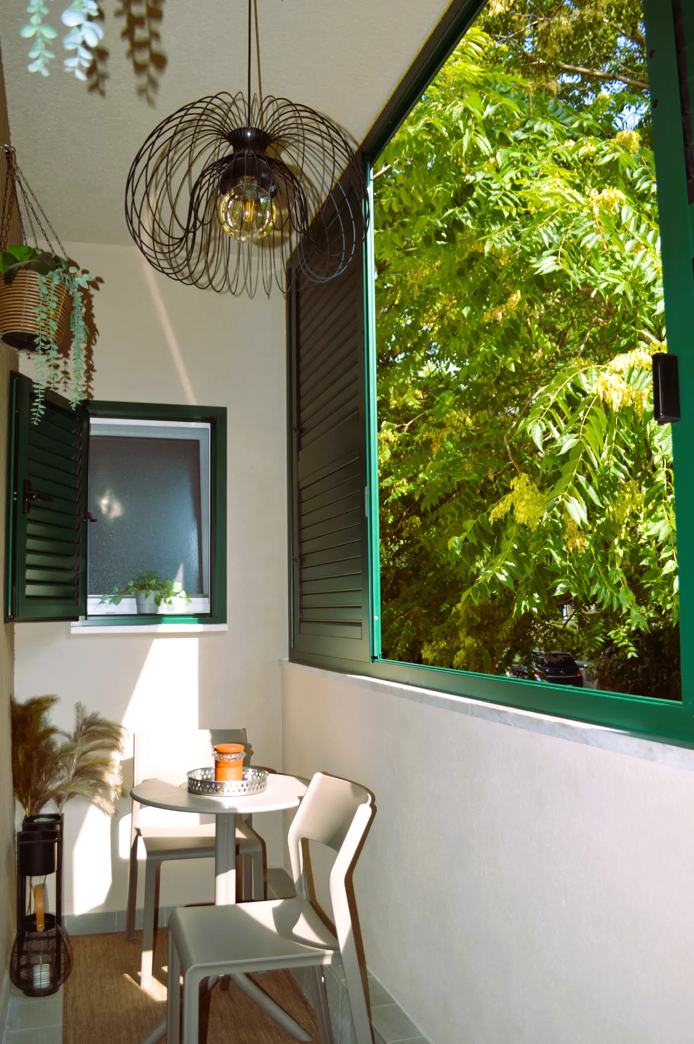 The balcony: a small table and two chairs, green shutters and a tree canopy