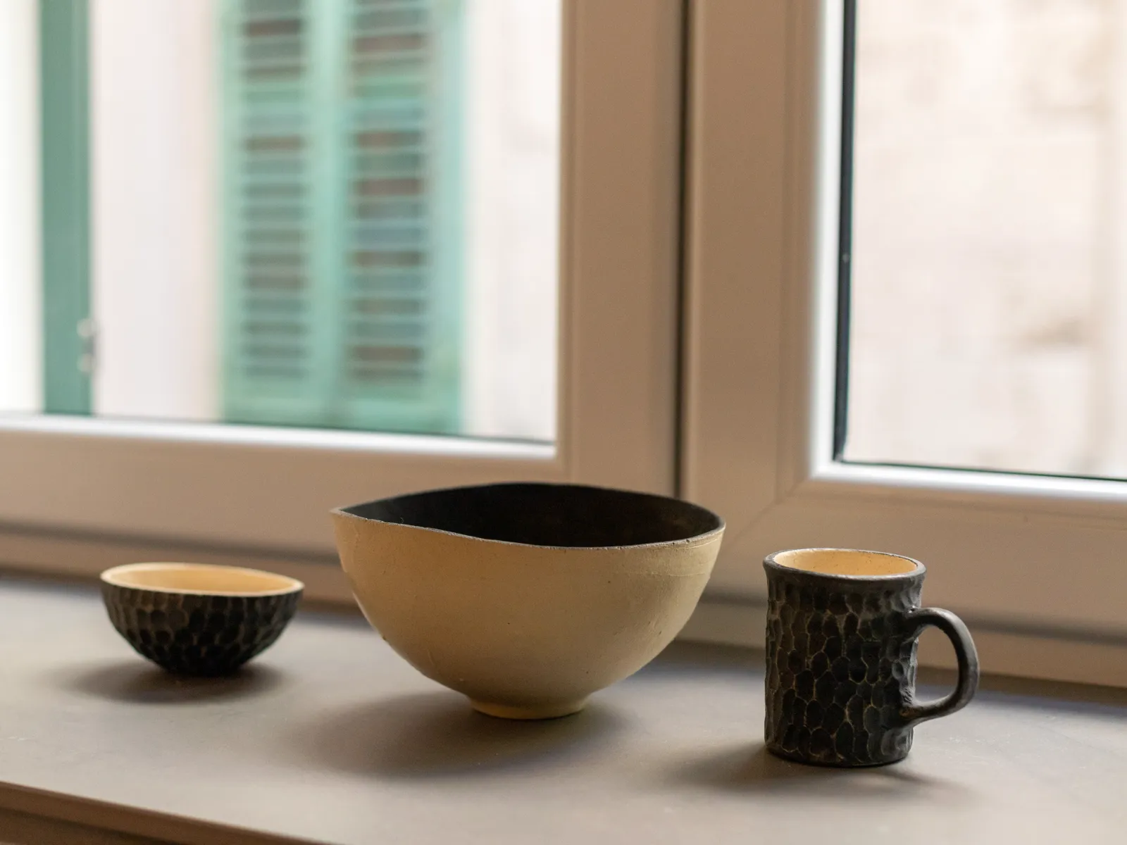 Ceramic bowls on the windowsill, a green shutter beyond