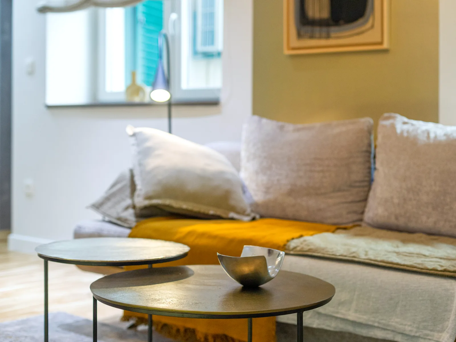 Sofa with an ochre throw and two round brass-toned side tables