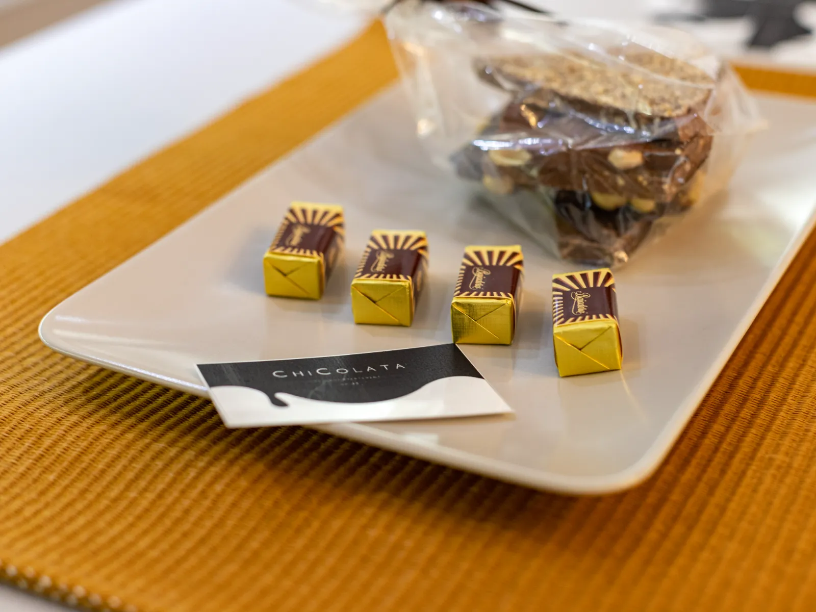 Chocolates and the ChiColata card on a plate, on an ochre placemat
